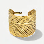 Damenarmreif mit breiter, strukturierter Metalloberfläche und offener Form, in Gold- oder Silberoptik am Handgelenk und in Detailansicht dargestellt